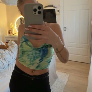 Grön och blå fest-topp Gina Tricot - Säljer en snygg fest-topp från Gina Tricot i storlek S. Toppen har ett grönt och blått mönster, är croppad och knyts i nacken och ryggen. Perfekt för sommaren med sin ärmlösa och öppna rygg-design. Materialet är lätt och känns skönt mot huden. En defekt av smink fläck men på insidan så syns inte vid användning. Använd 1 gång på festival 🌵