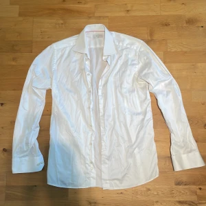 Vit slim fit skjorta från Eton - Klassisk vit skjorta från Eton i slim fit-modell. Skjortan har lång ärm, bred krage och knappar framtill. Tillverkad i bomull med snygga manschetter. (Sitter som en liten Large)