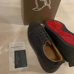 Christian Louboutin  bruna  sneakers - Snygga svarta sneakers från Christian Louboutin i mocka med klassisk röd sula och diskret logga. Skorna har rund tå, platt sula och snörning. Perfekta för dig som vill ha en lyxig och stilren look med en ikonisk touch.