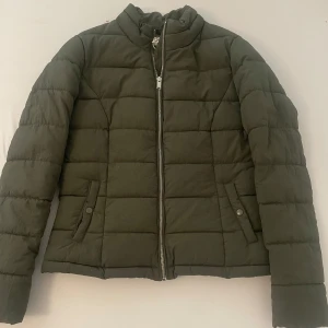 Olivgrön pufferjacka från ONLY - Säljer en olivgrön pufferjacka från ONLY i storlek S Jackan har quiltad design, hög krage, dragkedja framtill och två fickor med knappstängning. Perfekt för kyliga dagar och riktigt snygg till jeans eller cargo. Har också en till i storlek xs!