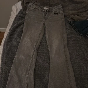 Grå bootcut jeans från Gina Tricot - Säljer ett par grå jeans från Gina Tricot i storlek 164. Jeansen har bootcut-modell med utsvängda ben, klassisk femficksdesign och dragkedja med knapp framtill. Materialet är denim och färgen är snyggt tvättad grå.