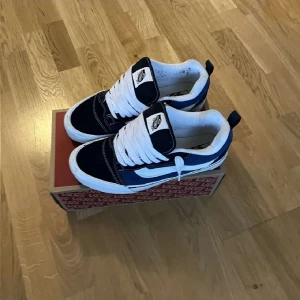 Svartvita Vans sneakers med snörning - Säljer ett par klassiska Vans sneakers i svart och vitt med tydliga vita snören och den ikoniska sidoremsan. Skorna har rund tå, platt sula och är tillverkade i canvas och mocka. Perfekta för dig som gillar streetstyle och skatekänsla.