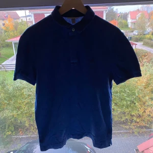 Blå pikétröja från Lacoste  - Säljer en klassisk blå pikétröja från Lacoste i storlek L. Tröjan har korta ärmar, krage med två knappar och den ikoniska broderade krokodilen på bröstet. Tillverkad i mjuk bomull med lite stretch för skön passform.