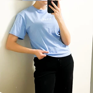 Blå t-shirt från Destination - Ljusblå t-shirt från Destination med trycket 'BLOOMING' i vitt framtill. Klassisk rund hals och korta ärmar. Tillverkad i 100% bomull för en skön och mjuk känsla. Perfekt för dig som gillar enkel och stilren design med en liten twist.