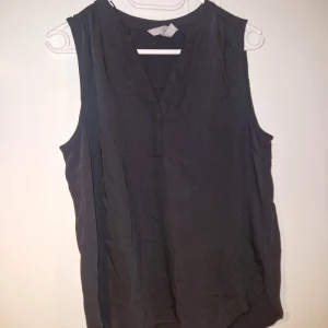 Svart ärmlös blus med v-ringning - En stilren svart ärmlös blus från H&M med v-ringad hals och avslappnad passform. Toppen är tillverkad i ett mjukt och lätt material, perfekt för varma dagar. Enkel design som funkar till många olika looks.