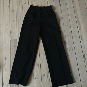Svarta vida byxor från H&M XS - Svarta byxor från H&M i storlek XS med hög midja och vida ben. Byxorna är tillverkade i stretchigt material med 93% polyester och 7% elastan, vilket gör dem bekväma och följsamma. Snyggt skräddad look med pressveck framtill. Sitter jätte fina runt midjan men var tyvärr för långa för mig!💕