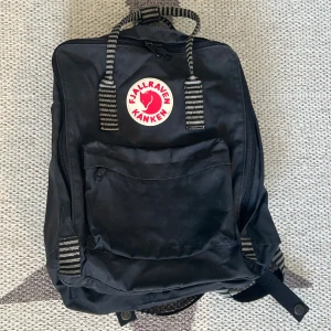 Svart randig Fjällräven Kånken ryggsäck - Klassisk svart randig Fjällräven Kånken ryggsäck i bra skick. Har bara lite skrapmärken på framfickan. Har också tagit bort namnteckning innanför. Sittdyna medföljer. 