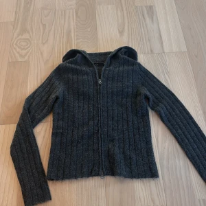 Mörkgrå ribbad hoodie från 157 - Mysig mörkgrå hoodie från 157 med ribbat stickat material och dragkedja hela vägen. Tröjan har huva och långa ärmar, perfekt för lager på lager.
