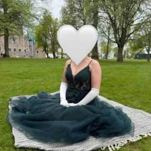 Mörkgrön balklänning med spetsdetaljer - Säljer en magisk mörkgrön balklänning med tunna axelband, v-ringad spetsliv och voluminös tyllkjol. Klänningen har broderade detaljer och transparenta partier upptill som ger en lyxig känsla. Perfekt för bal eller student! Använd en gång och i mycket fin skick, från Dream Design.