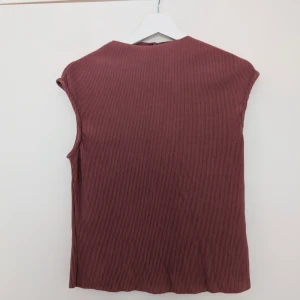 Ribbad ärmlös topp från NA-KD - Säljer en ribbad ärmlös topp från NA-KD i en mörkrosa nyans. Toppen har en rak passform och är tillverkad i ett mjukt, stretchigt material. Perfekt att styla med jeans eller kjol för en enkel och trendig look.