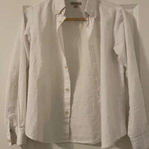 Vit skjorta från Burberry - Säljer en klassisk vit skjorta från Burberry i mycket bra skick. Skjortan har långa ärmar och knappar framtill. Perfekt för både vardag och festliga tillfällen. Den är gjord i ett bekvämt bomullsmaterial och har en stilren design.