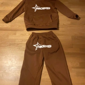 Bruna mjukisbyxor med tryck - Bruna mjukisbyxor från NOFS med vitt tryck och stjärndetalj framtill. Byxorna har resår i midjan och är tillverkade i mjukt material som känns skönt mot huden. Perfekta för chill dagar eller när du vill ha en avslappnad look.