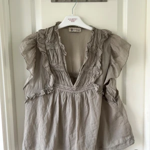 Grön aktiv blus med volanger från Chelsea - Säljer en grönaktig blus från Chelsea med djup v-ringning, volangdetaljer och broderade partier. Blusen har korta, luftiga ärmar.