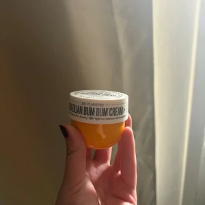 Sol de Janeiro Brazilian Bum Bum Cream - En ikonisk Brazilian Bum Bum Cream från Sol de Janeiro i en rund, gul plastburk med vitt lock. Den har en tropisk doft och är känd för sin återfuktande och mjukgörande formula. Perfekt för dig som vill ha glow och silkeslen hud.