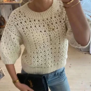 Vit stickad tröja med hålmönster - Superfin vit stickad tröja med hålmönster och bred ribbad kant vid hals, ärmslut och nederkant. Tröjan har en lite loose passform och trekvartsärmar som ger en chill vibe. Perfekt att styla med jeans eller kjol för en trendig look.