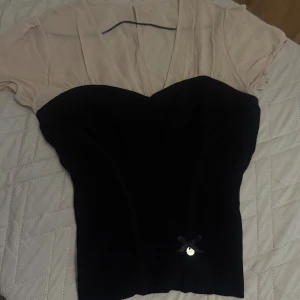 Svart och beige kortklänning med rosett karen millen - Supersnygg kortklänning med svart ribbad kropp och beige mesh upptill. V-ringad hals och korta ärmar ger en cool kontrast. Söt liten svart rosett med metallcharm framtill. Perfekt för dig som gillar unika detaljer och stilren look.