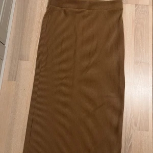 Brun ribbad långkjol med slits - Snygg brun långkjol med ribbad struktur och diskret slits bak. Kjolen har en rak passform. Mjuk och stretchig, passar till många olika outfits.