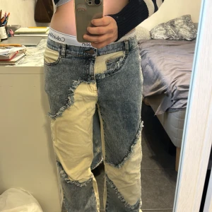 Patchwork jeans i beige och blå denim - Unika patchwork jeans med kontrasterande beige och blå denimtyg. Råa kanter och fransiga detaljer ger en cool, edgy vibe. Rak passform med klassisk femficksdesign och blå denimdetaljer på bakfickorna. Perfekta för dig som vill sticka ut.