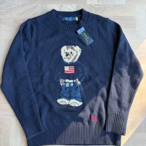 Ralph lauren stickad tröja NY - Säljer denna mörkblåa stickade tröjan från Polo Ralph Lauren med ikoniska Polo Bear-motivet framtill. HELT NY med tags på. Sjukt skön och perfekt nu till hösten. Storlek M. Hör av er vid eventuella frågor eller funderingar :)