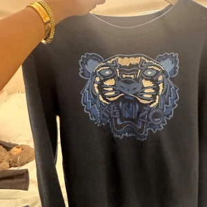 Mörkblå Kenzo tröja med tigerbrodyr - Kenzo tröja i mörkblått med ikonisk tigerbrodyr i blå och beige toner på bröstet. Mjuk insida och klassisk passform med rund hals och långa ärmar. Perfekt statement piece för dig som gillar streetstyle och vill sticka ut.
