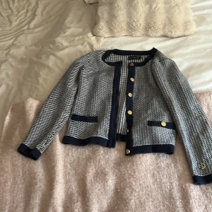 Mönstrad cardigan jacka/kofta från Stockh LM - Snygg cardigan jacka från Stockh LM i svart och vitt mönster. Jackan har guldiga knappar framtill och vid ärmslut, samt dekorativa fickor. Stickad känsla och rund halsringning ger en klassisk men trendig look.