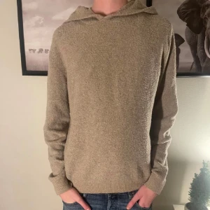 Beige stickad hoodie med huva - Mysig beige stickad hoodie med huva och långa ärmar. Tröjan har en enkel och stilren design med ribbade muddar vid ärmslut och nederkant. Perfekt för dig som gillar en avslappnad och chill stil.