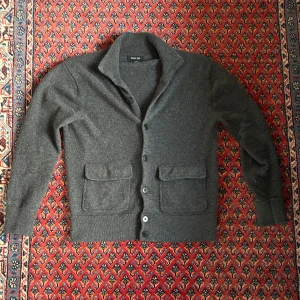 Massimo dutti cardigan - Säljer en stilren mörkgrå kofta från Massimo dutti med klassisk krage och stora fickor framtill. Står att det är storlek M men den har krympt lite så den sitter som Small. Den är i mycket bra skick och har inga defekter. Hör av er om ni undrar något mer! 