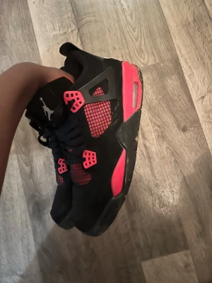 Nike Jordan 4 svart och röd sneakers - Säljer ett par Nike Jordan 4 sneakers i svart och röd färg med coola meshdetaljer och Jumpman-logga på hälen. Skorna har snörning, platt sula och är tillverkade i syntet och skinn. Perfekt för dig som gillar streetwear och vill sticka ut med en klassisk modell.