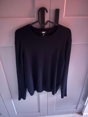 Mörkblå stickad tröja från Uniqlo - Säljer en stilren mörkblå stickad tröja från Uniqlo i storlek S. Tröjan har rund halsringning och långa ärmar, perfekt för lager-på-lager under kyliga dagar. Enkel design utan mönster eller detaljer, vilket gör den lätt att matcha med olika outfits.