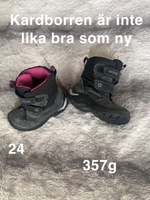 Svarta vinterstövlar från ECCO strl 24 - Säljer ett par svarta vinterstövlar från ECCO med rosa foder och blommiga detaljer. Stövlarna har kardborreband, grov platt sula och reflexdetaljer baktill. perfekt för kalla dagar.🌸 Använt skick.kardborren är inte lika bra som ny. Innermått ca 15cm. Storlek 24