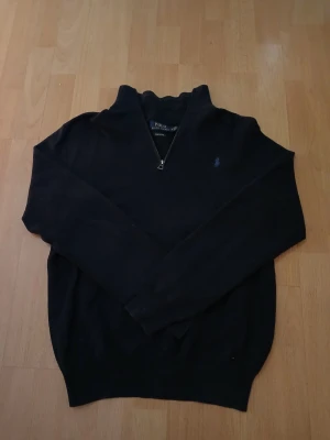 Mörkblå quarter zip tröja från Polo Ralph Lauren - Mörkblå långärmad tröja från Polo Ralph Lauren med quarter zip och broderad logga på bröstet. Tröjan är stickad och har en klassisk passform med hög krage. Perfekt för lager-på-lager och chill höst- och vinterstil. Bredd 45cm / Längd 60cm. Nypris: 2599kr / Mitt pris: 1199kr