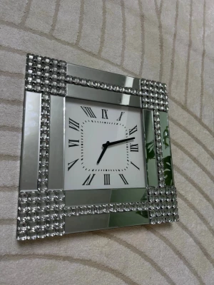 Glittrig väggklocka med spegel och stenar - Säljer en fyrkantig väst i silver med glittriga stenar och spegelpaneler. Västen har en lyxig vibe med dekorativa kristaller längs kanterna och en stilren, modern form. Perfekt för dig som gillar att sticka ut och vill ha något extra i garderoben.