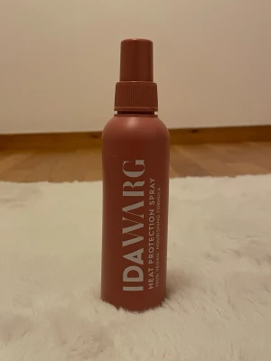 IDAWARG Heat Protection Spray - Snygg värmeskyddsspray från IDAWARG i en matt, rostrosa plastflaska med vitt tryck. Sprayen är vegansk och skyddar håret mot värme. Perfekt att använda innan styling med plattång eller locktång. Det är halva kvar av flaskan. Säljer till någon som verkligen gillar IDA WARGS produkter och behöver värmeskydd ASAP för en billig slant. 