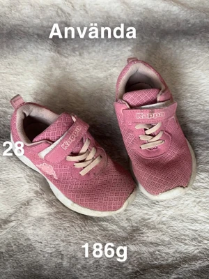 Rosa sneakers från Kappa, strl 28 - Säljer ett par rosa sneakers från Kappa med vit sula och ljusa snören. Skorna har kardborreband och ett diskret rutmönster på ovansidan. Perfekta för dig som gillar sportig stil och vill ha bekväma skor till vardags.🌸 Använt skick. Ej tvättade. Stl 28
