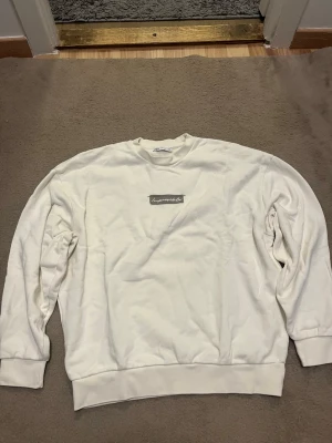 Vit sweatshirt från Zara med tryck - Vit sweatshirt från Zara i storlek S med ett grått tygmärke på bröstet där det står 'Impossible' i vit text. Tröjan har rund hals, långa ärmar och ribbade muddar vid ärmslut och nederkant. Perfekt för chill dagar och enkel att matcha med jeans.