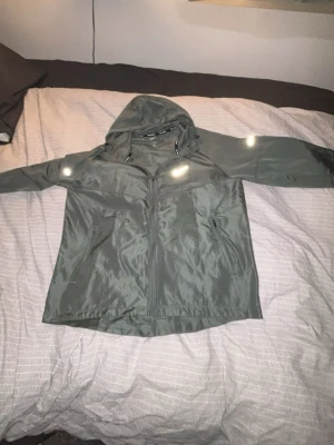 Grå nike Miller  - Nike vindjacka i grått med huva och dragkedja framtill. Jackan har reflekterande detaljer och snörning i huvan. Perfekt för löpning och träning, lätt och smidig att bära. Snygg Nike-logga på bröstet och insidan av huvan med texten 'NIKE RUNNING'.