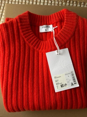 Filippa K Wool Rib Sweater Korallröd Strl.S - Ny stickad tröja från Filippa K.  Åtsittande tröja i en italiensk ullkashmirblandning med markerad vertikal ribbstruktur.  Made in: Romania Material: 90% Wool (RWS), 10% Cashmere  Strl.Small (normal i storlek)  Nypris 2700kr  Se gärna mina övriga annonser för bundlerabatter och samfrakt!