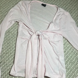 Ljusrosa omlottopp från Gina Tricot - Säljer en ljusrosa omlottopp från Gina Tricot i storlek XXS. Toppen har långa ärmar, djup v-ringning och knyt framtill. Materialet känns mjukt och lätt, perfekt för vår och sommar. Supersnygg att styla med jeans eller kjol!