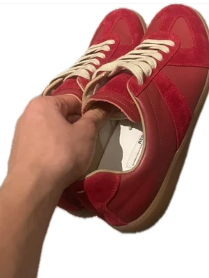 Tryck på bilden! Maison Margiela röda sneakers - Maison Margiela sneakers i rött med beige snörning och gummisula. Skorna har en mix av mocka och skinn på ovandelen, rund tå och platt sula. Klassisk design med diskret logga på sulan och snygga kontraster mellan material och färger.