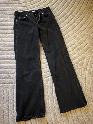 Svarta bootcut jeans från NA-KD - Säljer ett par svarta jeans från NA-KD med bootcut-snitt och låg midja. Jeansen har klassisk femficksdesign, knapp och dragkedja fram samt ett NA-KD-märke bak i midjan. Materialet är jeans i bomull med lite stretch för skön passform. Lite användning därav pyttelite slitage vid hälen.