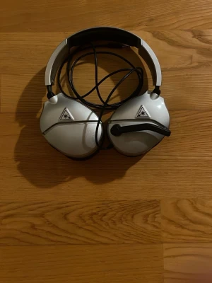 Turtle Beach kabelanslutet spelheadset - Kabelanslutet Turtle Beach spelheadset med mikrofon, silverfärgat. Passar perfekt för gaming och har tydlig logotyp på båda kåporna. Skicket ser bra ut, inga synliga defekter eller större slitage. Perfekt för dig som vill ha bra ljud och kommunikation under spel.