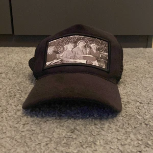 Velvet keps  - Säljer en svart velvet keps med mesh på sidorna och baksidan. Framtill finns en svartvit patch med ett retro foto på Kungens familj. Kepsen har justerbar snapback och en liten metallogo på sidan. Perfekt accessoar för en cool streetstil.