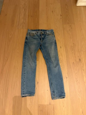  Nudie gritty jackson Jeans - Säljer ett par klassiska blå jeans från Nudie Jeans med fem fickor och snygga detaljer på bakfickorna. Jeansen har rak passform och normal midja, tillverkade i slitstarkt bomullsmaterial.  31/32 i storlek