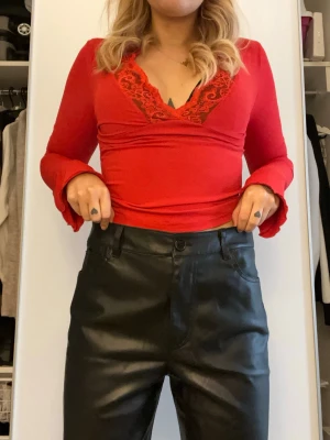 Svarta raka byxor i skinnimitation - Säljer ett par svarta byxor i skinnimitation med raka ben och klassisk femficksdesign. Byxorna har midjehöjd med knapp och dragkedja framtill samt bälteshällor. Snyggt glansigt material som ger en cool vibe och passar perfekt till sneakers eller boots. Dom är lite stora på mig så bilden kan vara lite missvisande 