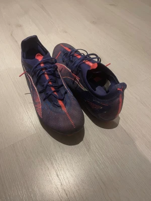 Puma Ultra blå/röda fotbollsskor - Snabb leverans och priset kan vi snacka om.            Säljer ett par Puma Ultra fotbollsskor i mörkblå och röd färg med snygga detaljer och snörning. Skorna har en smal och sportig form med rund tå och platt sula med dobbar för gräsplan. Ovandelen är tillverkad i syntetmaterial för lätt vikt och bra känsla på bollen.
