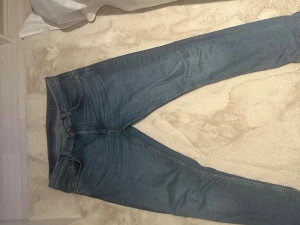 Nudie Jeans Lean Dean - Säljer ett par blå skinny jeans från Nudie Jeans med klassisk orange söm och snygga detaljer på bakfickorna. Jeansen har normal passform, fem fickor och är gjorda i mjukt bomullsmaterial. Perfekt för dig som gillar stilrena och bekväma jeans.