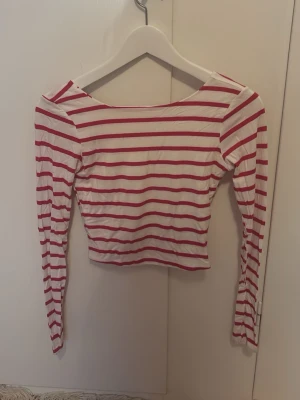 Randig långärmad topp från Amisu - Säljer en vit och röd randig långärmad topp från Amisu i storlek XS. Toppen har en bred, rundad halsringning både fram och bak och är croppad i modellen. Materialet är mjukt och stretchigt, perfekt för en chill och snygg look.