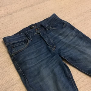 Slim Glenn jeans från Jack & Jones - Snygga blå jeans från Jack & Jones, modell Slim Glenn. De har en slim passform med klassisk femficksdesign och subtila slitningar för en cool look. Jeansen är tillverkade i stretchigt denim för extra komfort och har normal midja.