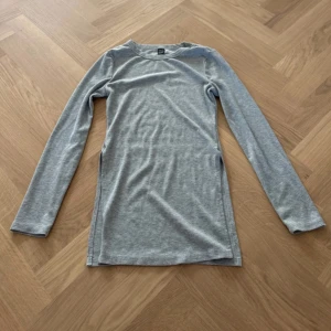 Grå ribbad långärmad tröja  Shein - En enkel och stilren grå klänning från Shein i ribbad bomull. Modellen är långärmad och har en rund halsringning. Klänningen är kort och har en slim passform som sitter snyggt på kroppen. Perfekt för dig som gillar minimalistisk och clean stil.