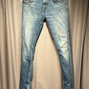 Blå slim jeans från Tiger of Sweden - Snygga blå jeans från Tiger of Sweden med klassisk femficksdesign och kontrastsömmar. Modellen är skinny med smal passform och har ljus tvätt med slitningar på framsidan. Perfekt för dig som gillar stilrena och moderna jeans.